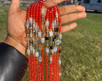 May include: A long strand of beaded jewelry with red, white, and gold beads. The beads are arranged in a repeating pattern.