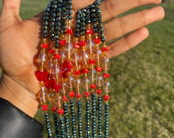 May include: A multi-strand beaded necklace with dark green, gold, and red beads. The necklace is made of faceted beads and has a layered design.