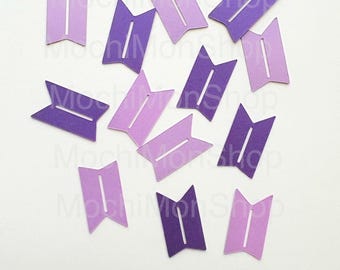 May include: A collection of purple and lavender paper cutouts, each shaped like a stylized flag with a vertical white stripe. The cutouts are scattered on a white surface, creating a visually appealing arrangement.