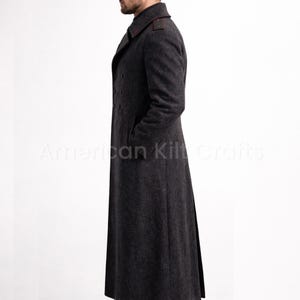 May include: A charcoal gray, double-breasted coat with a long silhouette. The coat features a notched collar with red accents and a row of dark buttons. The image shows the coat from the side, highlighting its tailored fit and classic design.