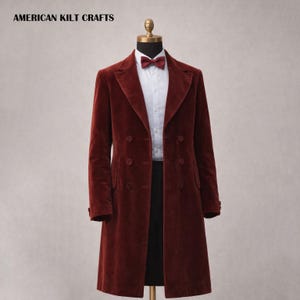 May include: A burgundy velvet overcoat with a double-breasted design, displayed on a mannequin. The coat features a notched lapel, two rows of buttons, and a long, tailored silhouette. A white dress shirt and burgundy bow tie are visible beneath the coat. The text "AMERICAN KILT CRAFTS" is at the top.