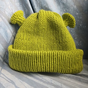Peut inclure: Un bonnet en tricot vert avec deux oreilles en forme d'oreilles d'ogre.