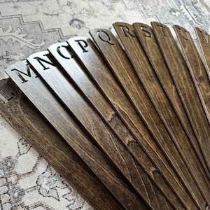 May include: A wooden alphabet fan with letters L through V, painted in a dark brown stain.