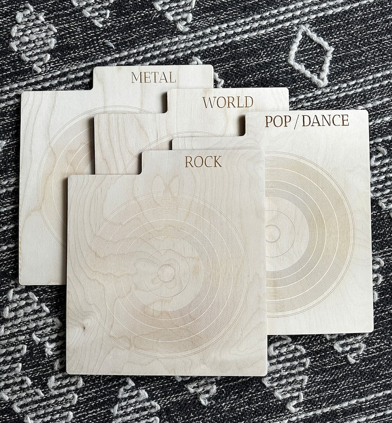 May include: A set of four light-colored wooden record dividers with tabs labeled METAL, WORLD, POP/DANCE, and ROCK. Each rectangular divider features a laser-engraved concentric circle pattern resembling a vinyl record, with a smooth finish.