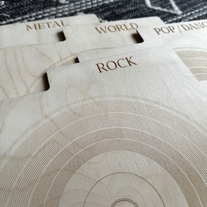 May include: A set of light-colored wooden record dividers featuring laser-engraved text labels including METAL, WORLD, POP/DANCE, and ROCK. Each divider has a tabbed top edge and a circular groove pattern resembling a vinyl record surface.