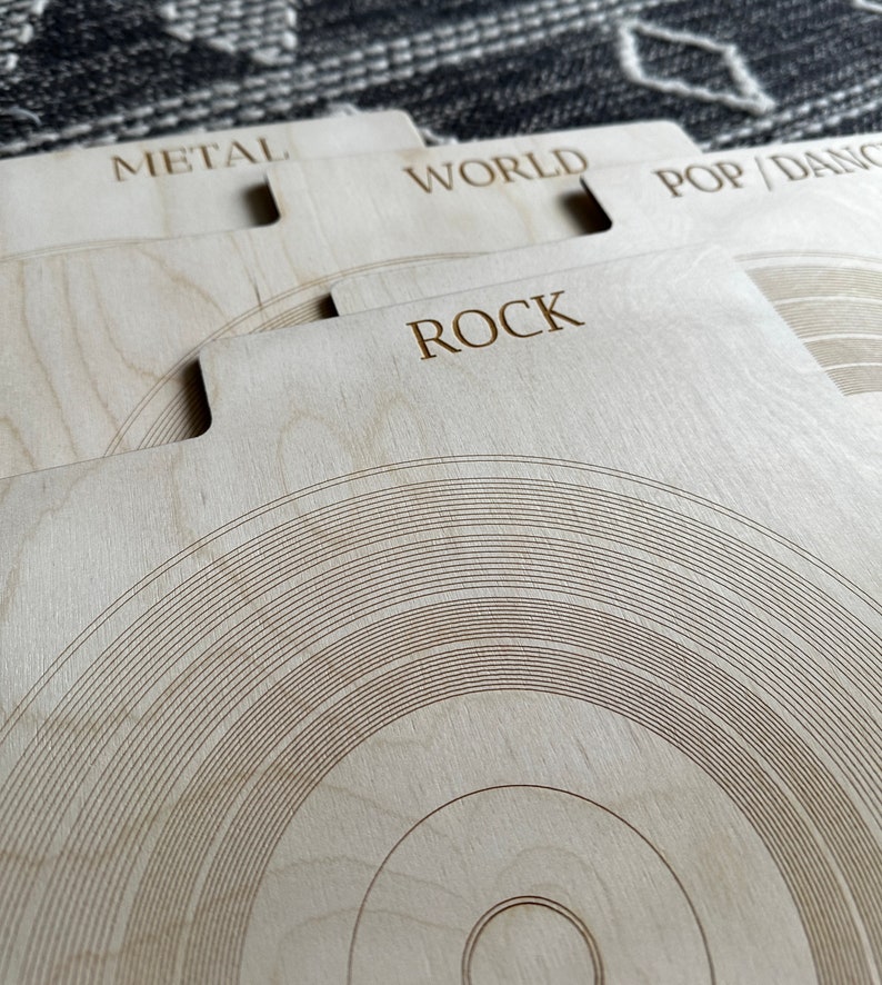 May include: A set of light-colored wooden record dividers featuring laser-engraved text labels including METAL, WORLD, POP/DANCE, and ROCK. Each divider has a tabbed top edge and a circular groove pattern resembling a vinyl record surface.