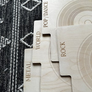 May include: A set of light-colored wooden record dividers with engraved text labels reading POP/DANCE, WORLD, and METAL, and ROCK. Each divider features a circular etched pattern resembling a vinyl record, organized in a stepped, overlapping arrangement.
