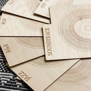 May include: A set of light-colored wooden record dividers featuring engraved concentric circle patterns and genre labels including Gospel, Hip-Hop, Pop, R&B, Soundtrack, Jazz, and Soft Rock, arranged in a fanned-out overlapping display.