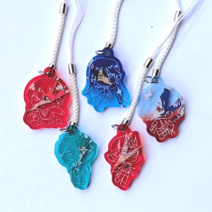 Puede incluir: Cinco colgantes acrílicos coloridos con cordones blancos. Los colgantes presentan diseños de personajes de estilo anime en rojo, azul y turquesa. Cada colgante tiene un cierre de metal plateado.