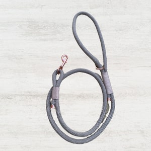 Könnte beinhalten: Eine graue Hundeleine aus Seil mit einem roségoldenen Metallclip. Die Leine ist aus geflochtenem Seil gefertigt und hat eine Schlaufe am Ende zum Befestigen an einem Halsband.