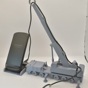 May include: A grey 3D printed model of a crane with a black phone charging stand. The phone stand has the text "NANAMI FAST CHARGE" on it.