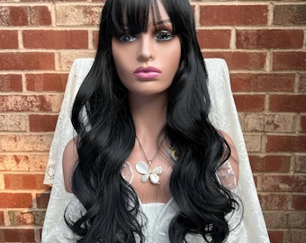 May include: A long, black wig with loose waves and bangs. The wig is styled on a mannequin head and has a butterfly necklace.
