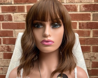 May include: A brown wavy bob wig with bangs. The wig is on a mannequin head and has a natural-looking finish.