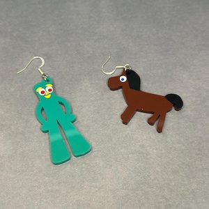 K&ouml;nnte beinhalten: Ein Paar Ohrringe mit einem gr&uuml;nen Comic-Charakter und einem braunen Pferd. Die Ohrringe sind aus Acryl und haben silberne Haken.