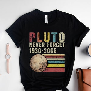 May include: Black t-shirt with a vintage-style graphic that says "Pluto Never Forget 1930-2006" and features a stylised image of Pluto with a rainbow stripe background.