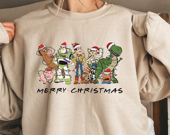 Può includere: Felpa beige con una grafica di personaggi animati con cappelli di Babbo Natale e luci natalizie. Il testo "MERRY CHRISTMAS" è stampato sotto. Un capo d'abbigliamento festivo per le vacanze.