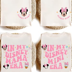 May include: Two white t-shirts with a pink Minnie Mouse design. One shirt says "Disney Mama" and the other says "Disney Mini". The bottom two shirts are the same design but say "In My Disney Mama Era" and "In My Disney Mini Era".