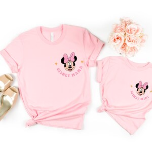 May include: Two pink t-shirts with a Minnie Mouse graphic. The larger shirt says "Disney Mama" and the smaller shirt says "Disney Mini".