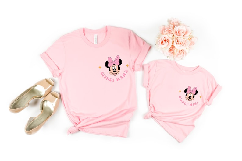 May include: Two pink t-shirts with a Minnie Mouse graphic. The larger shirt says "Disney Mama" and the smaller shirt says "Disney Mini".