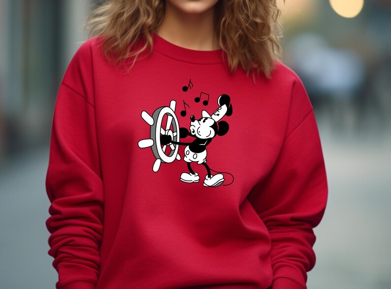 May include: Red sweatshirt featuring a black and white cartoon character, holding a ship's wheel and musical notes. The character is in a classic animated style. The sweatshirt is a solid red color.