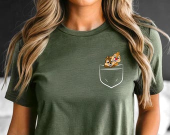 Puede incluir: Camiseta verde oliva con un diseño de bolsillo blanco con una imagen de dibujos animados de Chip y Chop. Los personajes de dibujos animados son marrones con narices rojas y asoman por el bolsillo.