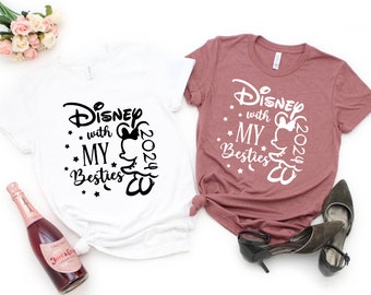 May include: Two t-shirts with a white background and a pink background. The white shirt has black text that says "Disney with my besties 2024" with a Mickey Mouse silhouette. The pink shirt has white text that says "Disney with my besties 2024" with a Mickey Mouse silhouette.