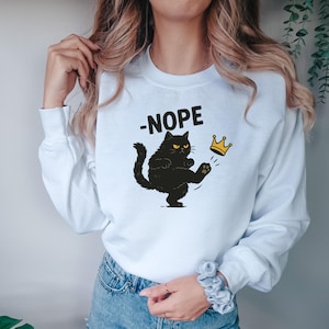 May include: White sweatshirt with a black cat graphic kicking a gold crown. The word "-NOPE" is printed above the cat. The cat has yellow eyes and is kicking the crown with its paw.