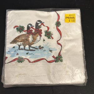 May include: A pack of white paper napkins with a Christmas design featuring two geese with red bows and holly. The pack has a yellow price tag that reads "Michaels 80227 £1.82"