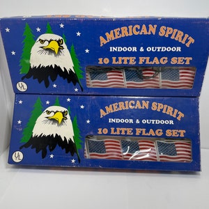 Puede incluir: Dos cajas de luces navideñas American Spirit 10 Lite Flag Set. Las cajas son azules con un águila calva blanca y estrellas. Las cajas dicen "American Spirit Indoor & Outdoor 10 Lite Flag Set".