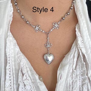 May include: A silver-toned necklace with a heart-shaped pendant. The necklace features a delicate chain with small beads and ornate floral accents. The text "Style 4" is visible in the image.