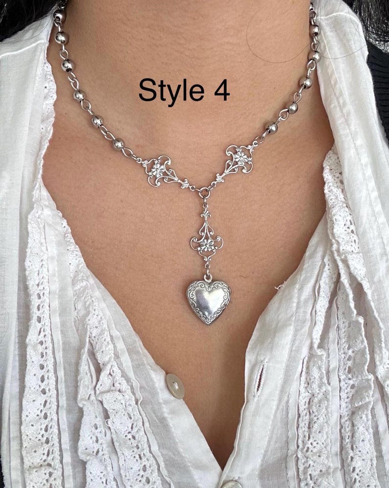May include: A silver-toned necklace with a heart-shaped pendant. The necklace features a delicate chain with small beads and ornate floral accents. The text "Style 4" is visible in the image.
