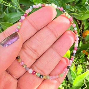May include: A delicate beaded bracelet featuring small, faceted, multi-coloured tourmaline gemstones in shades of pink, green, and clear, interspersed with tiny, polished gold-tone metal spacer beads arranged in a circular pattern.