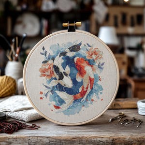Könnte beinhalten: Ein Kreuzstich-Stickrahmen mit einem Aquarell-Design von zwei Koi-Fischen, die in einem Kreis schwimmen. Die Fische sind weiß und schwarz sowie orange und rot mit blauen und weißen Aquarell-Akzenten.