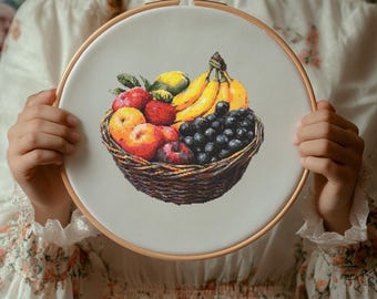 Puede incluir: Un bastidor de bordado de punto de cruz con una cesta de frutas. La cesta está llena de plátanos, uvas, manzanas y limones. El bordado está en un bastidor de madera.