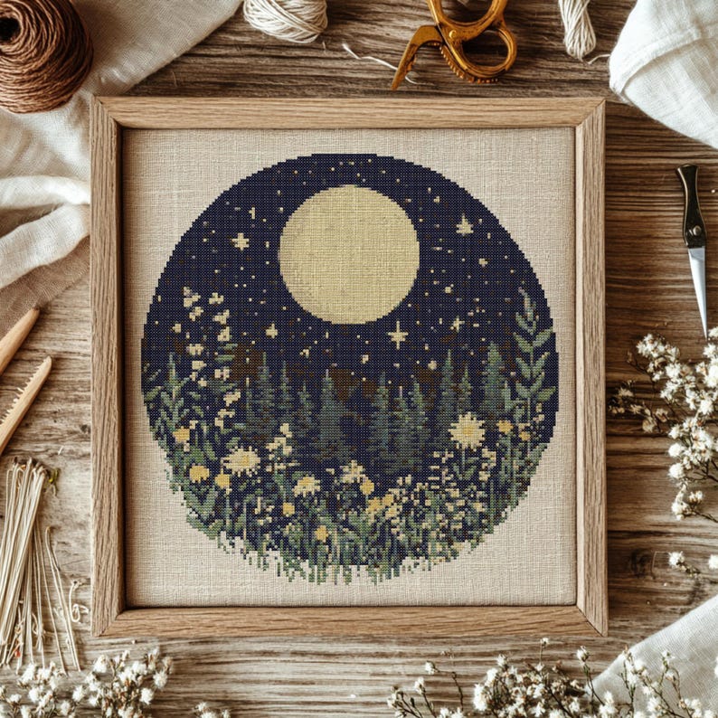 May include: A cross-stitch pattern featuring a full moon, stars, and a forest scene with flowers. The design is circular and has a dark blue background.