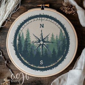 May include: A cross-stitch embroidery of a compass with a forest scene in the background. The compass is surrounded by a dark blue circle with the letters N and S for North and South.