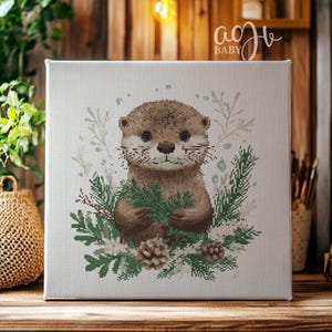 May include: A cross-stitch pattern featuring a cute brown otter holding a sprig of green leaves. The otter is surrounded by a wreath of green leaves and white flowers. The background is a light beige canvas.