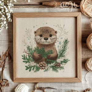 May include: Cross stitch pattern featuring a cute otter holding green leaves, surrounded by a wintery floral design. The pattern is framed in a light brown wood frame.