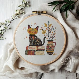 May include: A cross-stitch pattern featuring a black cat sitting on a stack of books with a vase of flowers behind it. The cat has yellow eyes and a happy expression. The books are decorated with colorful patterns. The vase is decorated with a geometric pattern.