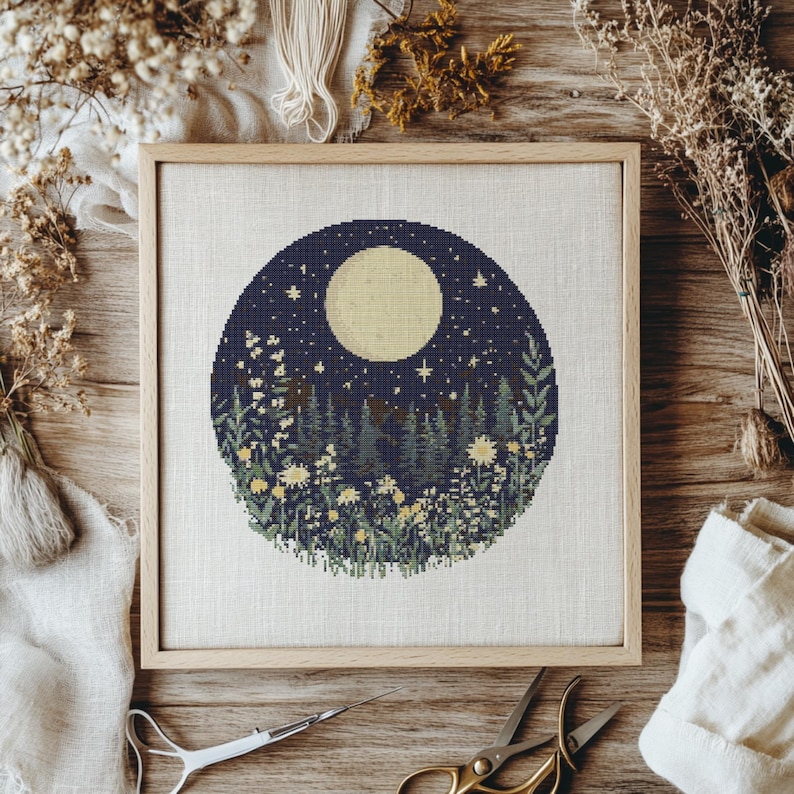 May include: A cross-stitch embroidery design featuring a full moon, stars, and a forest scene with flowers. The design is framed in a light wood frame.