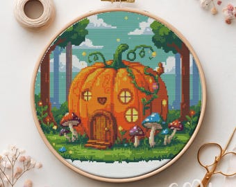 May include: Cross-stitch embroidery in a wooden hoop features a whimsical pumpkin house with a smiling door and round windows. The scene includes colorful mushrooms, trees, and a light blue sky, creating a fairy tale theme.