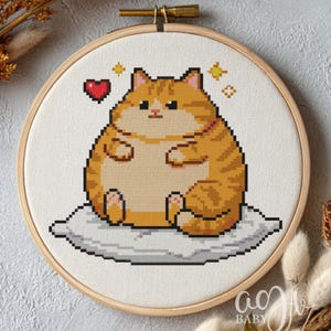 May include: A cross-stitch embroidery of a ginger tabby cat sitting on a cloud-like pillow. The cat has a heart and star accents. The embroidery is set in a wooden hoop, ideal for home decor.