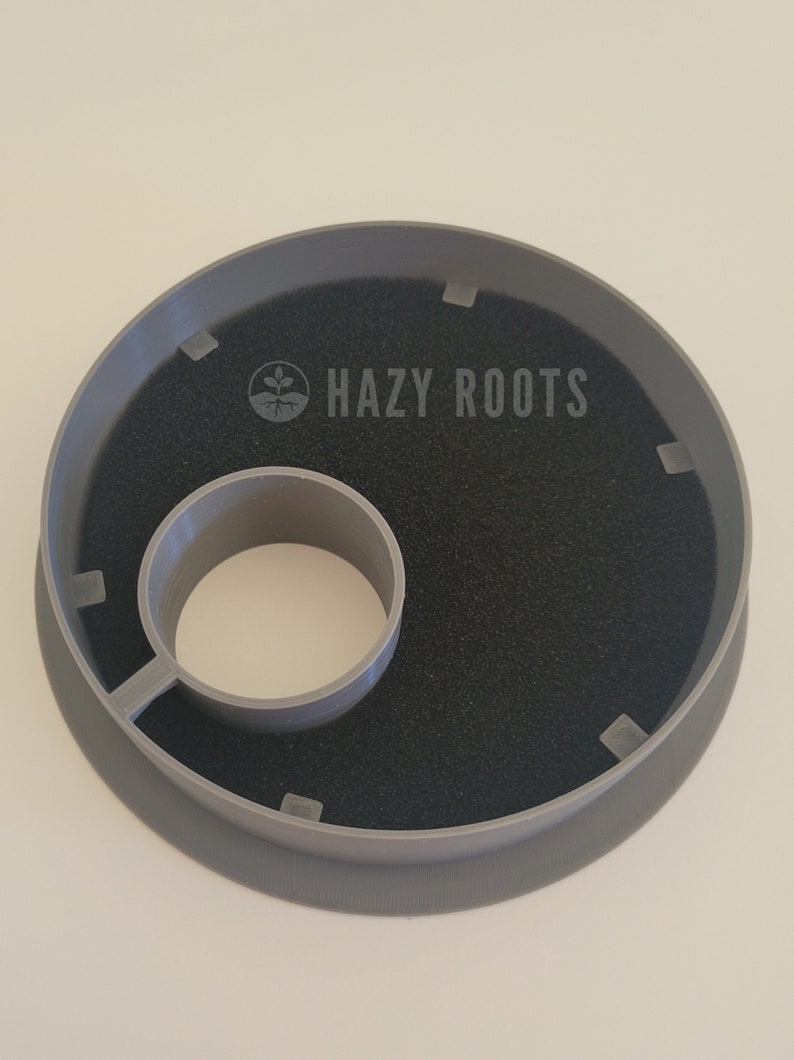 May include: Gray plastic plant pot saucer with a black foam insert and a central hole. The saucer has the text "HAZY ROOTS" printed on it.