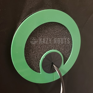 May include: A green circular grommet with a black foam insert and a black cable pass-through. The grommet is designed to protect cables from damage.