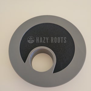 May include: Gray plastic ring with a black center and a hole in the middle. The ring has the text "HAZY ROOTS" printed on it.
