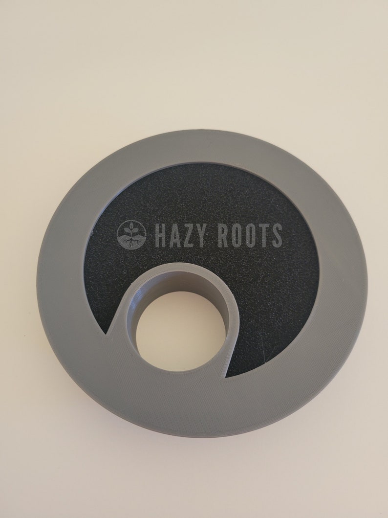 May include: Gray plastic ring with a black center and a hole in the middle. The ring has the text "HAZY ROOTS" printed on it.