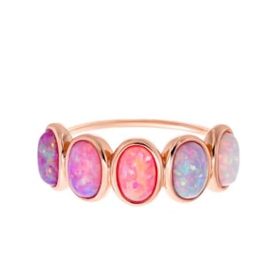 May include: A rose gold ring featuring five oval-shaped cabochon opals arranged in a row. The opals display iridescent flashes of pink, purple, and blue colors. The band is thin and polished, showcasing a metallic rose gold finish throughout.
