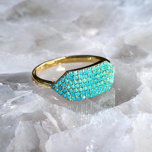 May include: A gold ring with a turquoise stone set in a unique, geometric shape.