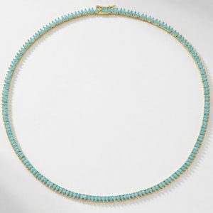 May include: A gold-toned necklace featuring a continuous row of small, teardrop-shaped turquoise-colored stones set in a metal frame. The necklace is arranged in a circular shape and includes a small metal clasp mechanism at the top center.