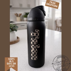 K&ouml;nnte beinhalten: Eine schwarze Owala-Wasserflasche mit einem karierten "Tabitha"-Design. Die Flasche hat einen schwarzen Griff und Deckel. Die Flasche steht auf einer wei&szlig;en Arbeitsplatte. Das Bild enth&auml;lt auch den Text "Versand in 5 Tagen oder weniger" und "Kostenloser Versand".
